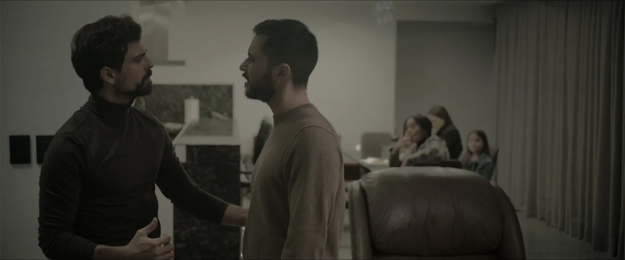 Los habitantes (2023) movie still: medium — A modern living area features neutral tones with a leather armchair in the foreground. Two men in casual…