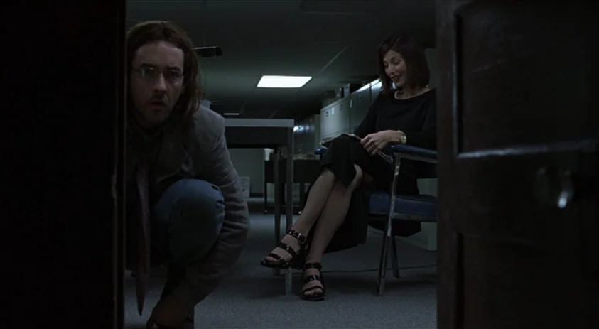 Being John Malkovich (1999) movie still: medium — A dimly lit backroom area contains rows of metal file cabinets under fluorescent lights. A man…