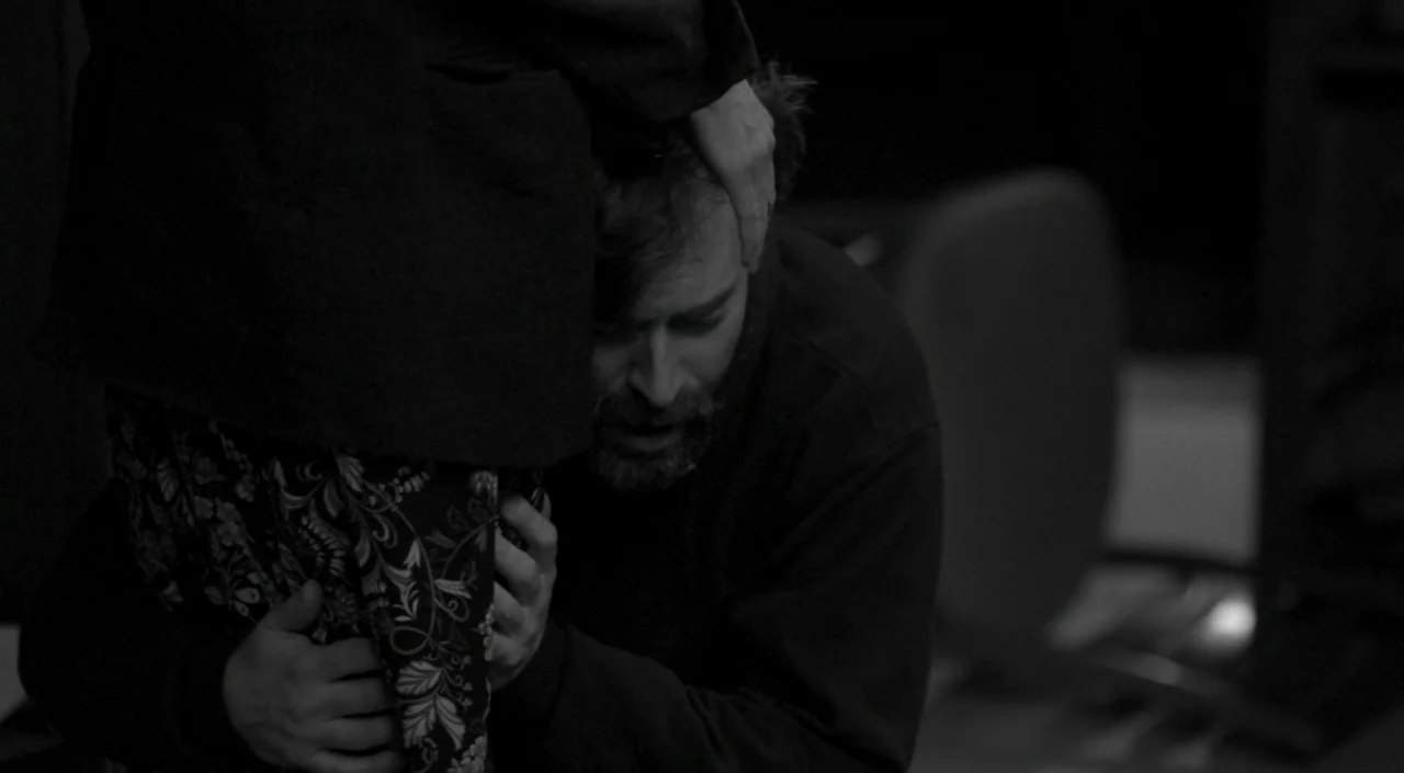 Blue Jay (2016) movie still: medium — A dark indoor space with minimal background detail visible in the shadows. A man with a beard kneels while…