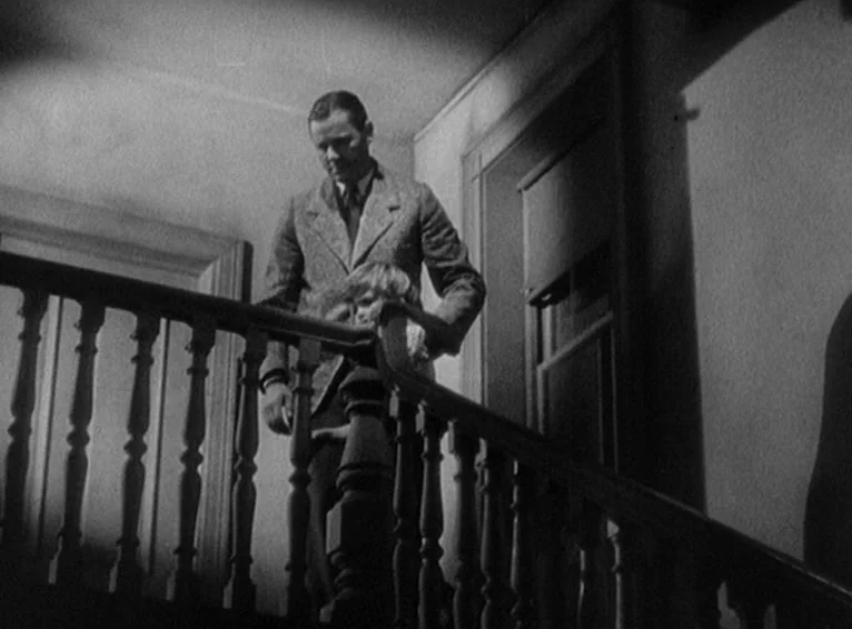 Blonde Venus (1932) movie still: medium — A man descends a wooden staircase carrying a child in his arms. The setting features classic banisters and…
