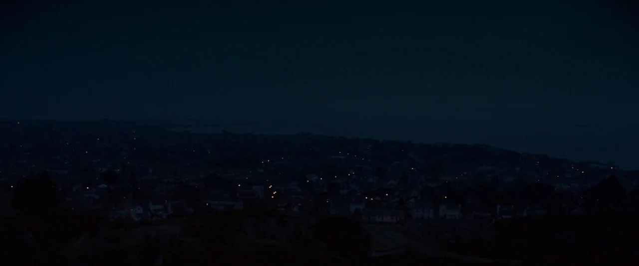 Kissing Candice (2017) movie still: establishing — A nighttime panoramic view of a seaside town with distant flickering residential street lighting.…