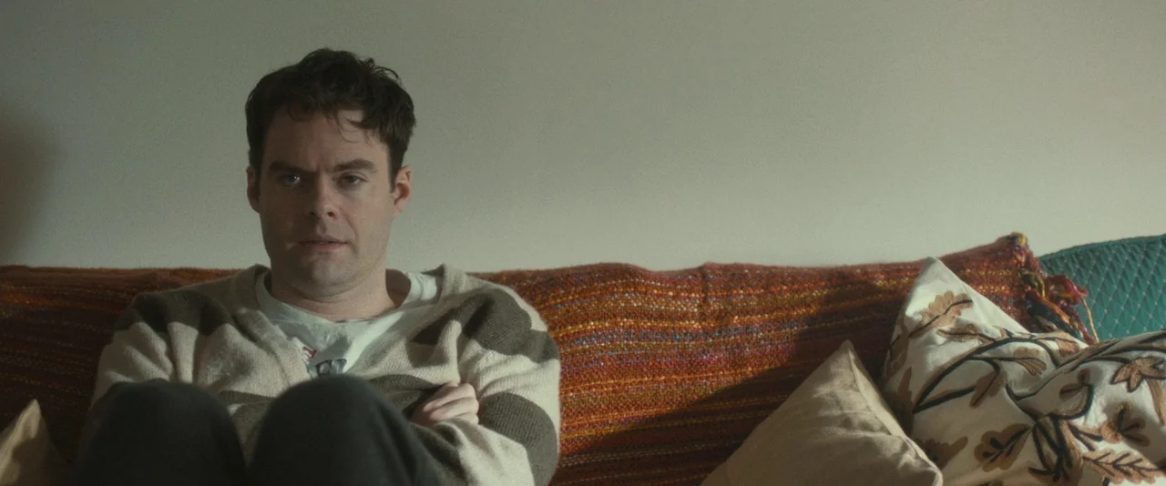 The Skeleton Twins (2014) movie still: medium — A man sits on a textile-covered sofa against a plain white wall. The man stares directly forward…