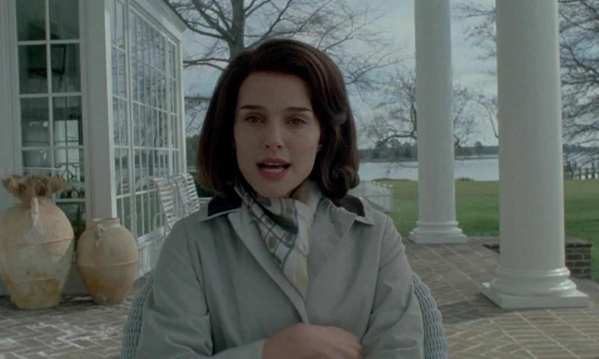 Jackie (2016) movie still: medium — A stone-paved veranda features white architectural columns and large decorative terracotta jars. A woman sits on…