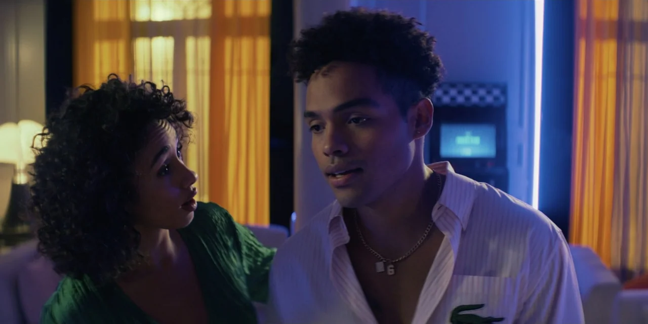 Our Fault (2025) movie still: medium — A dimly lit room features orange curtains and blue ambient light in the background. A woman in a green top…