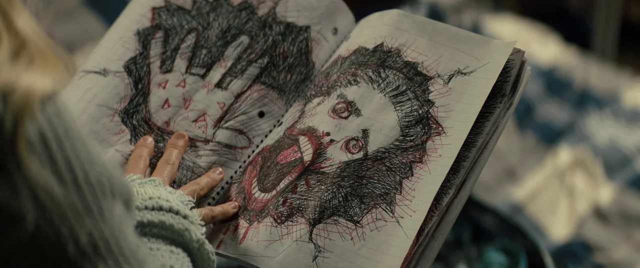 Brightburn (2019) movie still: closeup — An open notebook with intricate pen drawings rests in the hands of a person. The drawings depict a hand…