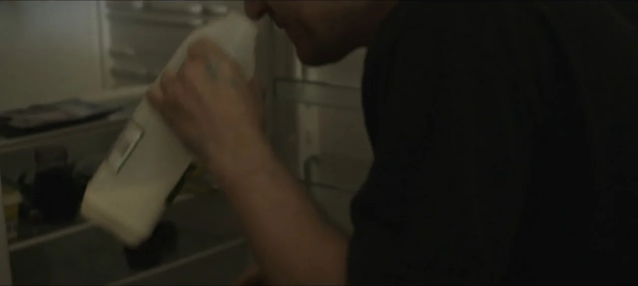 Containment (2015) movie still: medium — The interior of a refrigerator is visible with various food items stored on shelves. A man leans into the…