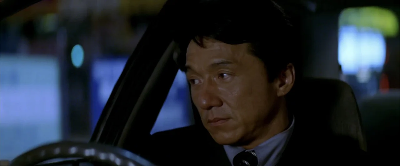 Rush Hour 2 (2001) movie still: closeup — A dark vehicle interior with a blurred nighttime city environment visible through the window. A man in a…