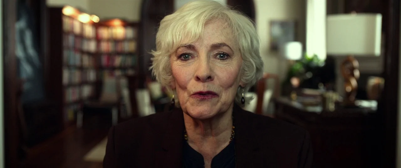 Split (2016) movie still: closeup — An interior space features shelves filled with books and a wooden desk. A woman faces the camera directly in a…