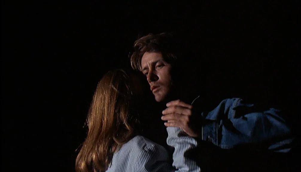 Badlands (1973) movie still: medium — A man and woman dance close together in complete darkness at night. The man in a denim jacket holds the woman…