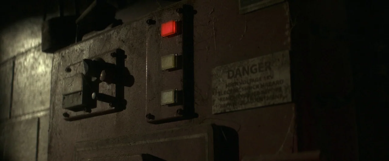 Ghostbusters: Afterlife (2021) movie still: closeup — An old, dusty metal electrical control panel is mounted on a dim wall surface. A single…