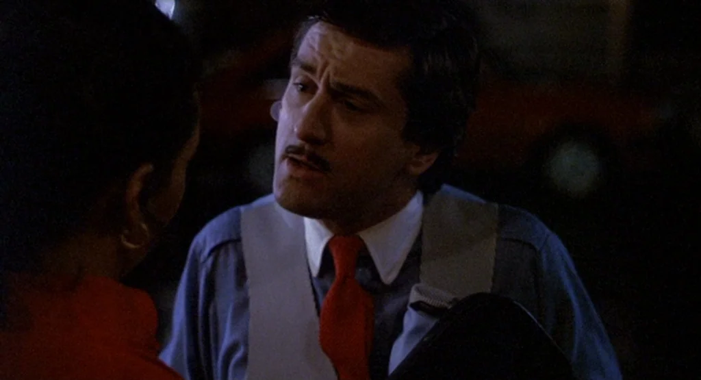 The King Of Comedy (1982) movie still: medium — A nighttime exterior scene featuring a man in a vest talking to another person. The lighting creates…