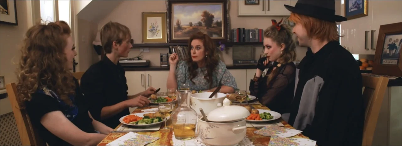 DannyBoy (2020) movie still: medium — Five individuals are seated around a wooden dining table set with white plates and serving dishes. The group…