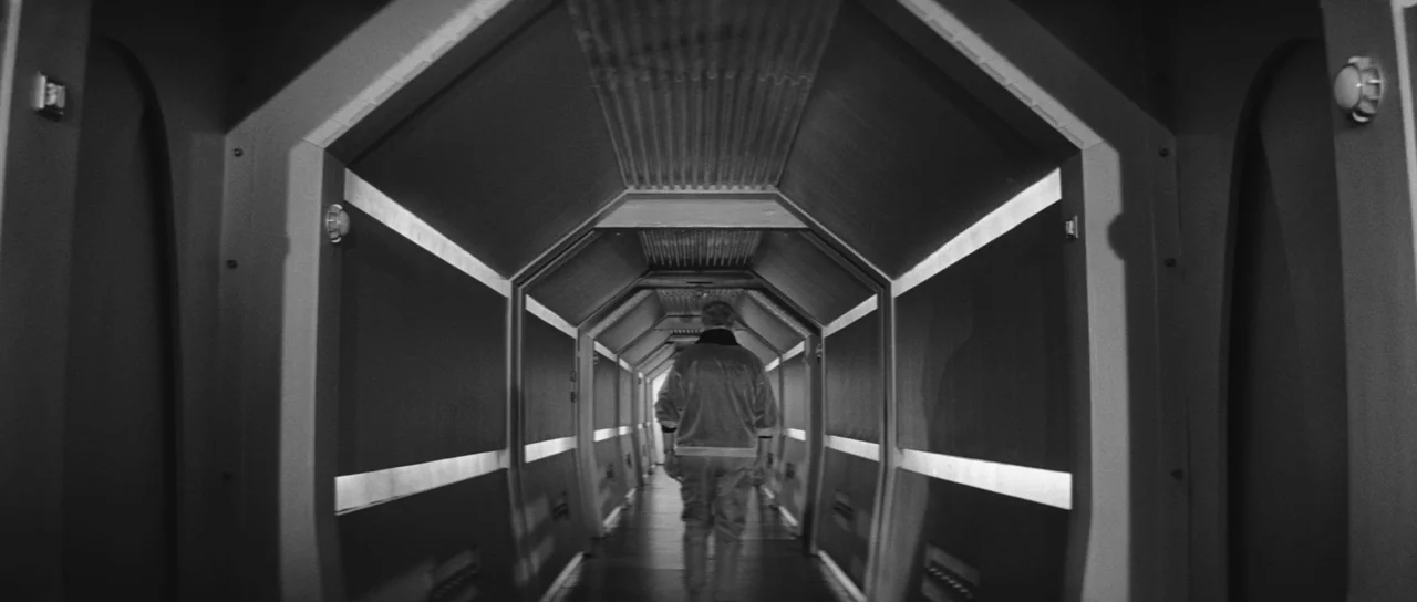 Ikarie XB 1 (1963) movie still: fullbody — A narrow, hexagonal spaceship corridor features repeating geometric wall panels and horizontal strip…