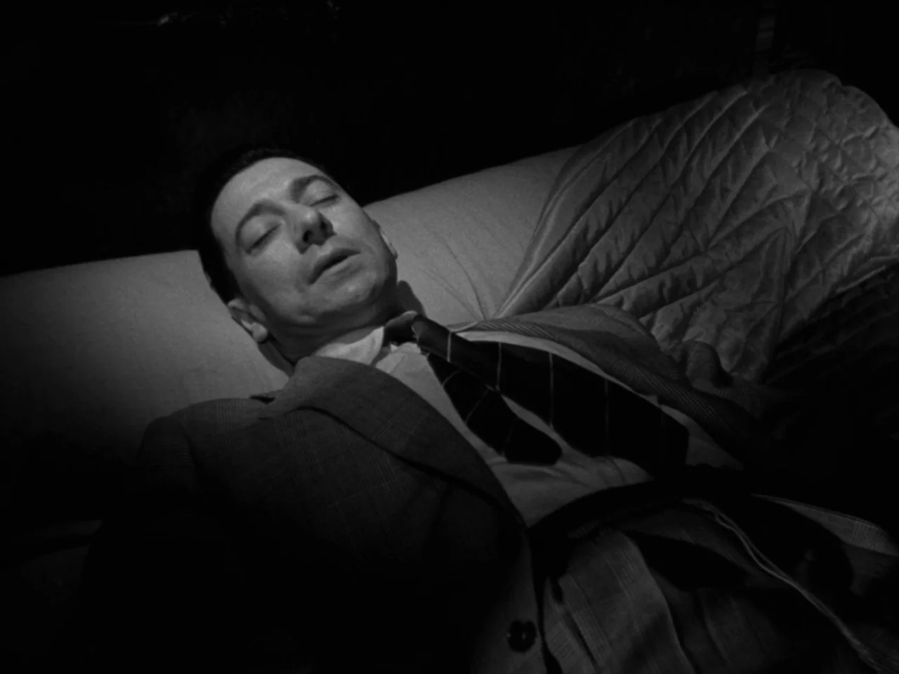 Diabolique (1955) movie still: closeup — A man rests on a quilted surface in a dark room. The sharp light focuses solely on his upper body and face.