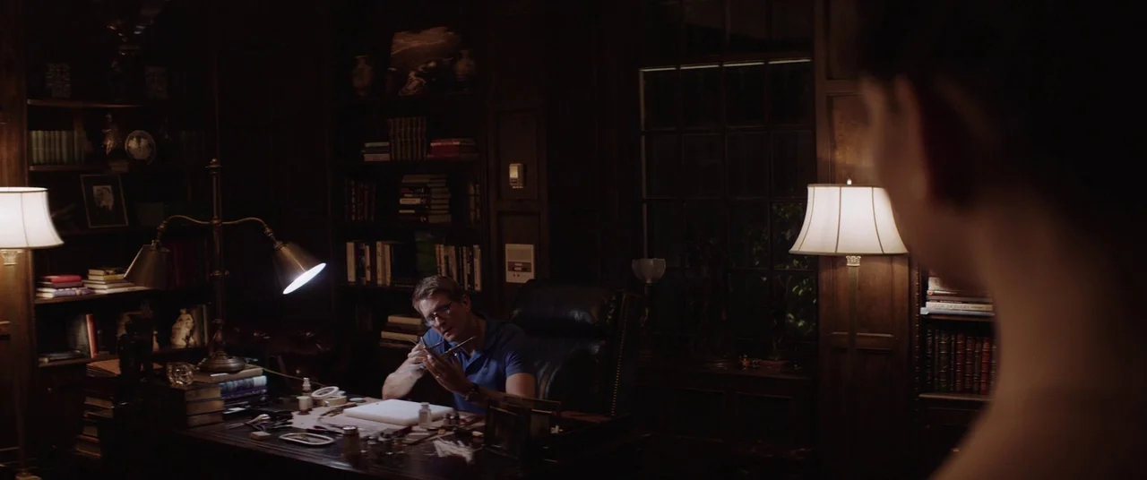Thoroughbreds (2017) movie still: wide — A dimly lit home office features wood paneling and extensive bookshelves surrounding a large desk. A man in…