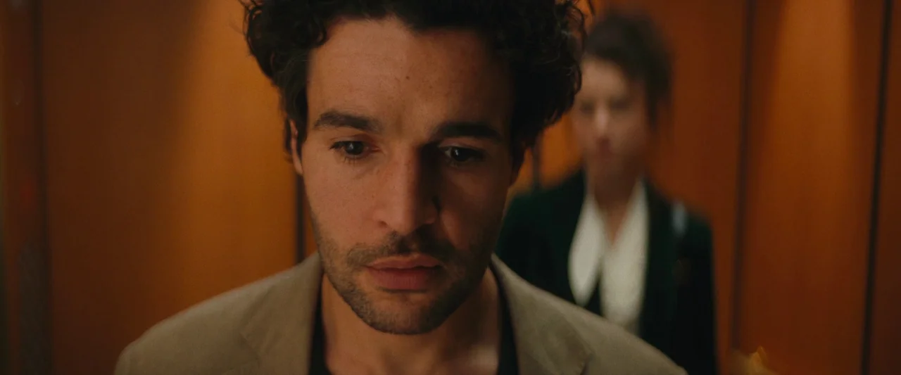 Sanctuary (2023) movie still: closeup — An elevator interior with wood-paneled walls and muted lighting. A man stands in the foreground with a woman…