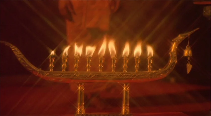 Boxer’s Omen (Mo) (1983) movie still: closeup — An ornate metal candle holder shaped like a boat sits on a surface. Nine small flames are lit,…