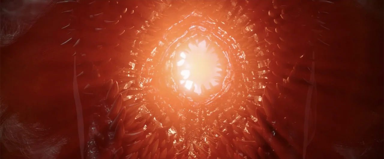 K.G.F: Chapter 2 (2022) movie still: closeup — A dark red organic tunnel lined with sharp, tooth-like structures curves inward. A blinding white…
