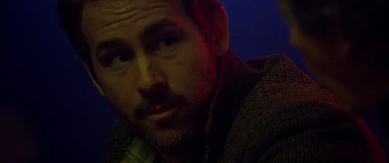 Mississippi Grind (2015) movie still: closeup — A dark environment is illuminated by contrasting neon blue and red lights. A man in a wool blazer…