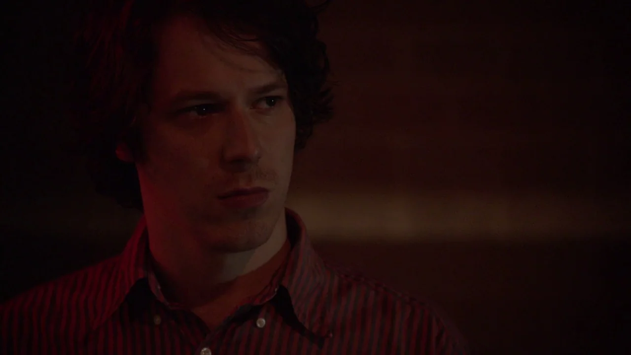 The Heart Machine (2014) movie still: medium — The subject stands in a darkened interior space with minimal architectural detail visible. The man in…