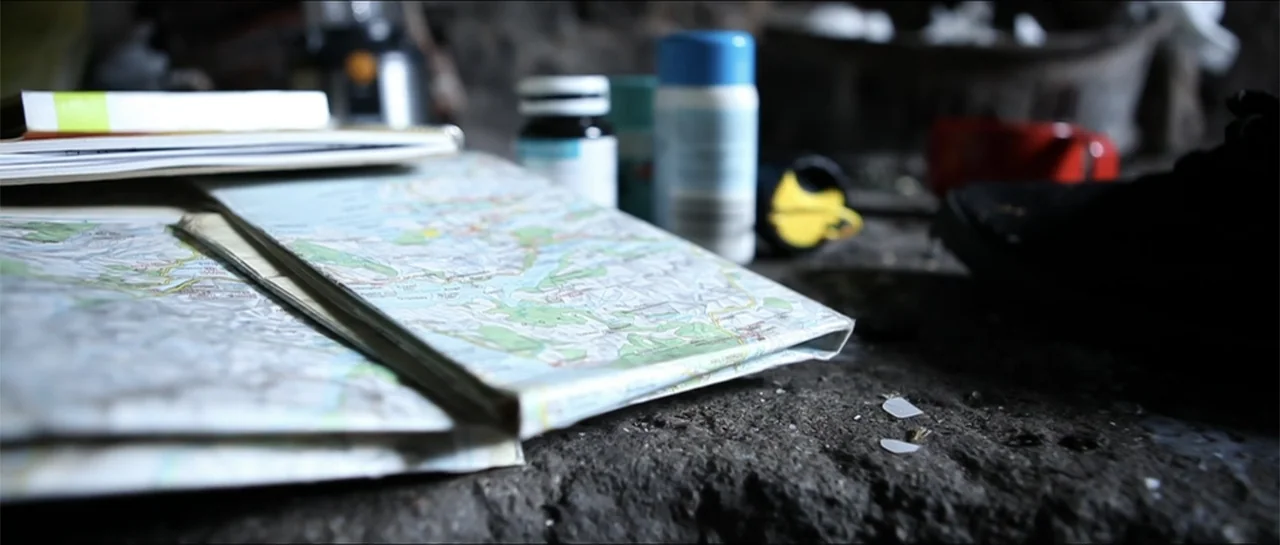Garnet’s Gold (2014) movie still: closeup — A folded road map rests on a rough, dark stone surface. Various small plastic bottles and a notebook are…