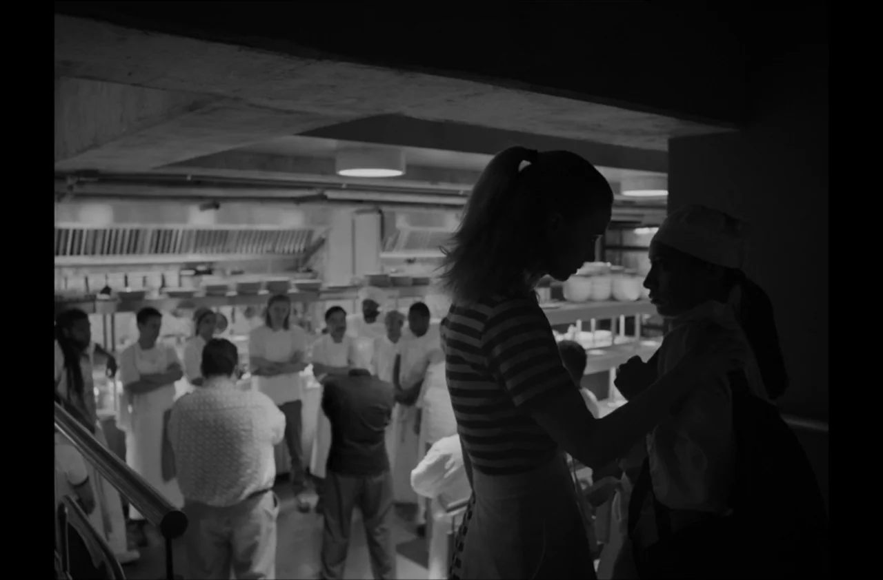 The Kitchen (2012) movie still: medium — A professional industrial kitchen area with stainless steel shelving and multiple staff members gathered.…
