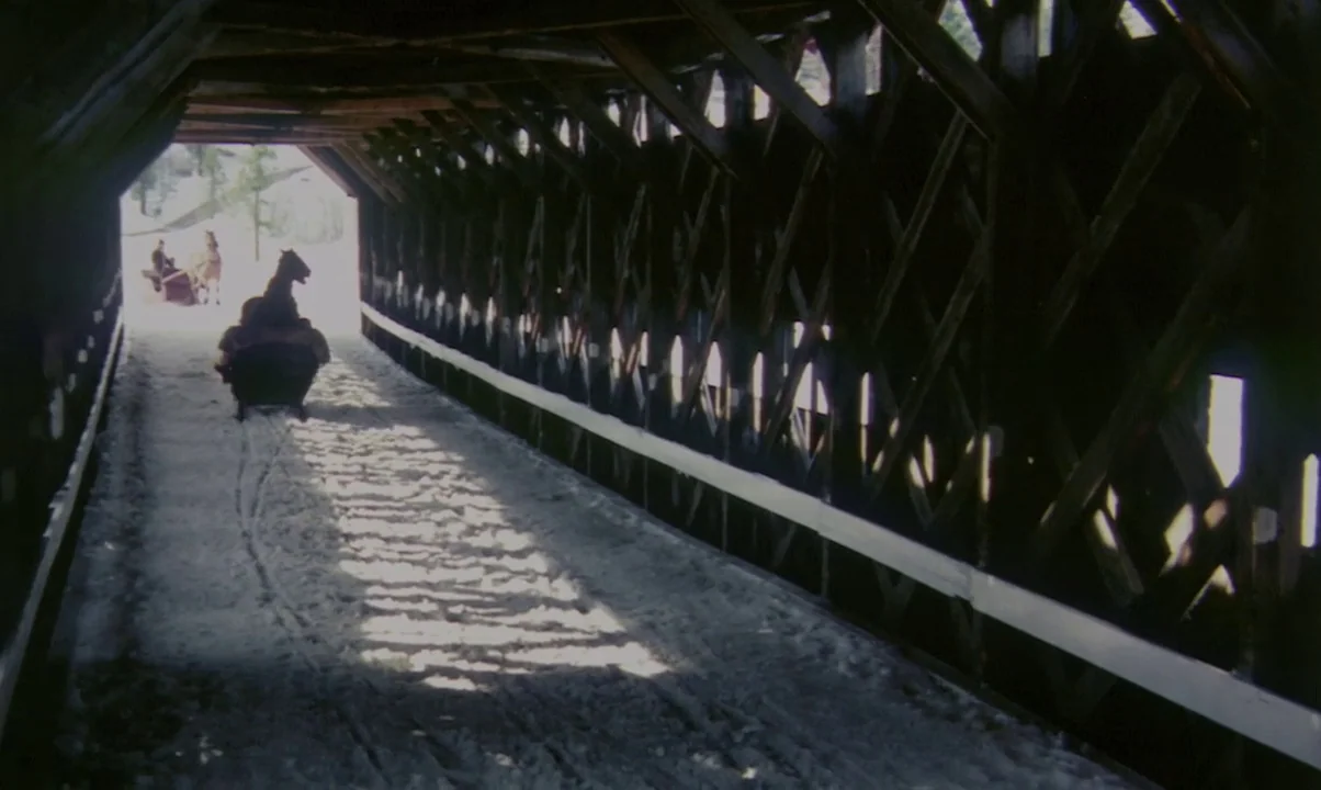 Kamouraska (1973) movie still: wide — A long wooden covered bridge features diagonal cross-bracing along the dark internal walls. A horse-drawn…