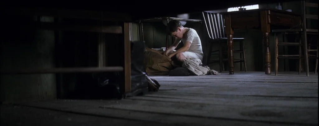 There Will Be Blood (2007) movie still: wide — A sparsely furnished wooden room contains a simple table, chairs, and a floor-level perspective. A…