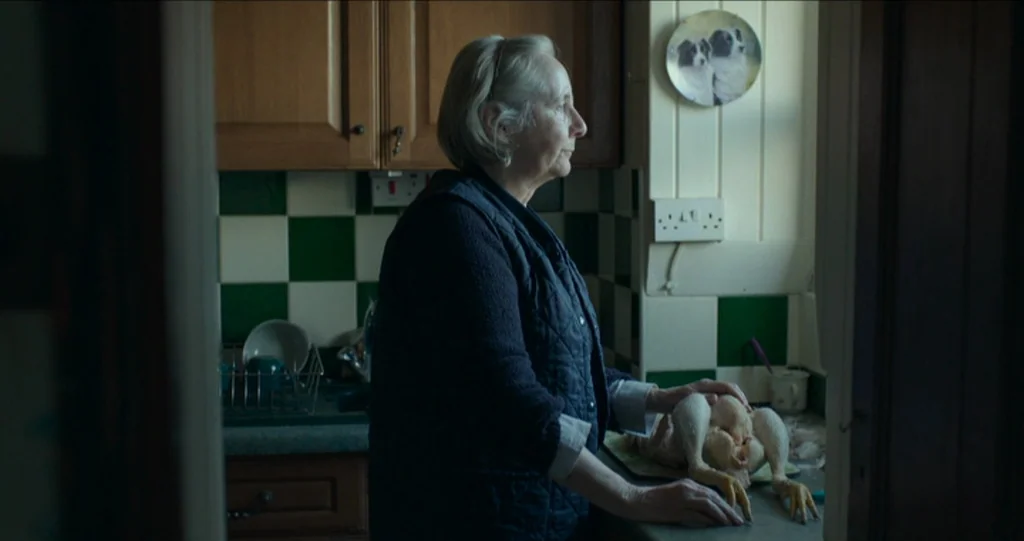 God’s Own Country (2017) movie still: medium — A residential kitchen features green and white checkered tiles above a countertop. An elderly woman…