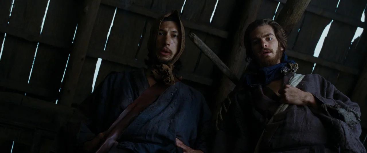 Silence (2016) movie still: medium — Two men stand inside a rustic wooden structure with weathered beams and planks above. They look down into the…