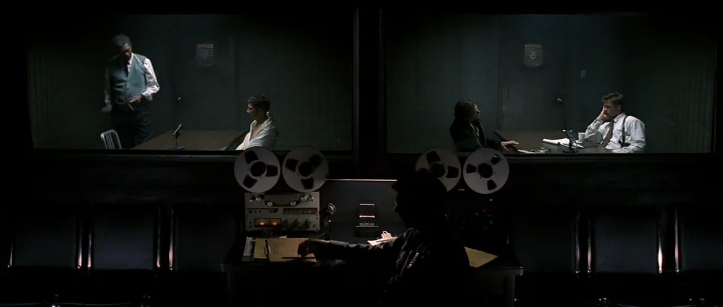Se7en (1995) movie still: wide — A dark observation room faces two glass-walled interrogation cells showing investigators and suspects. An obscured…