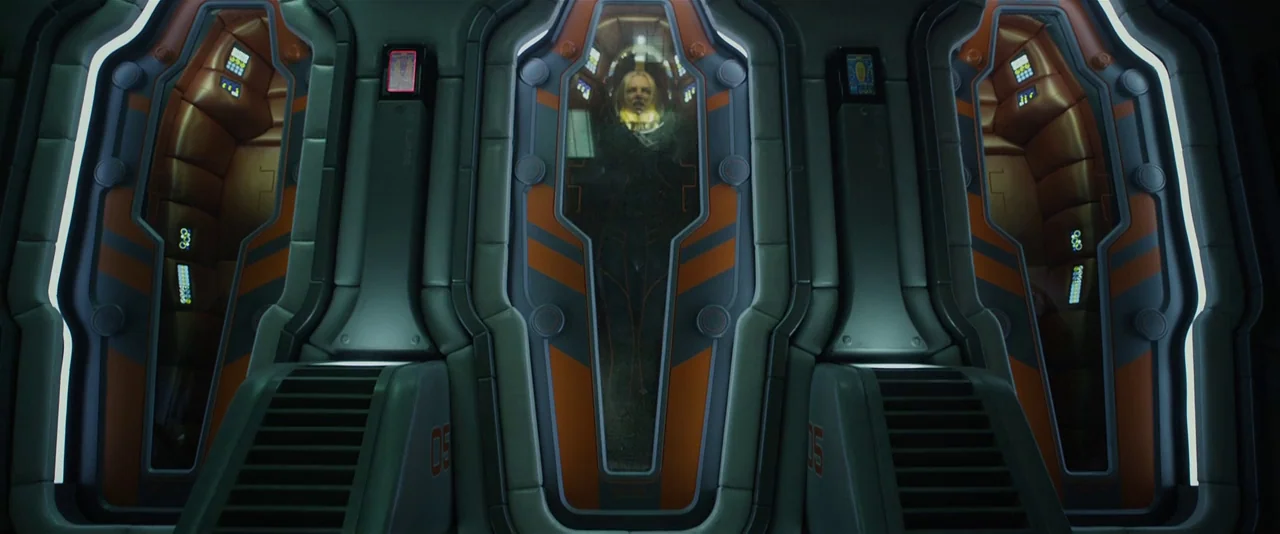 Prometheus (2012) movie still: wide — A row of futuristic, orange-accented cryogenic pods is mounted against a dark metallic wall. A woman rests…