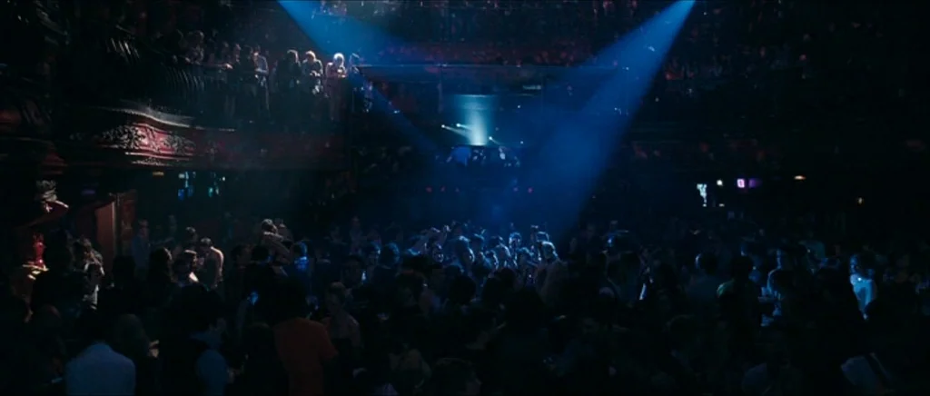 Happy-Go-Lucky (2008) movie still: wide — A crowded multi-level nightclub features a dance floor filled with people under spotlights. Deep shadows…