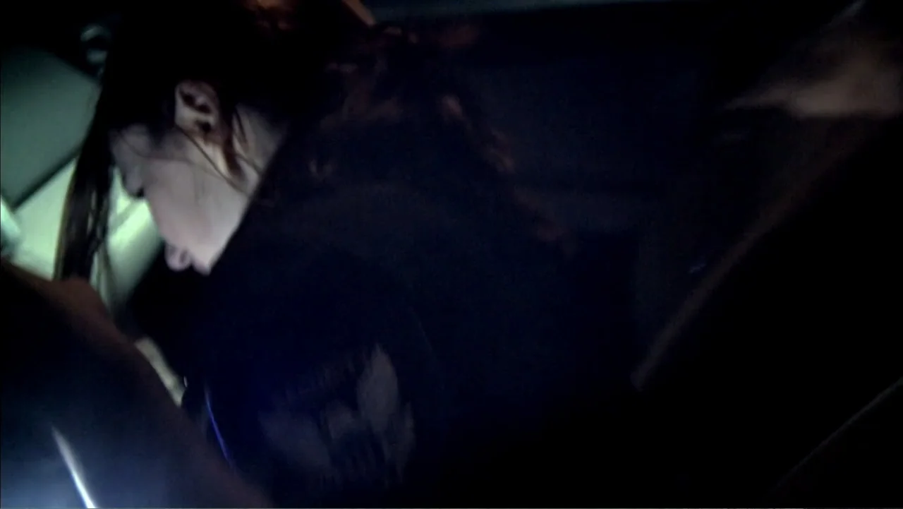 Abandoned Dead (2015) movie still: closeup — A dark vehicle interior with limited light visibility around the passenger or driver. A woman sits…