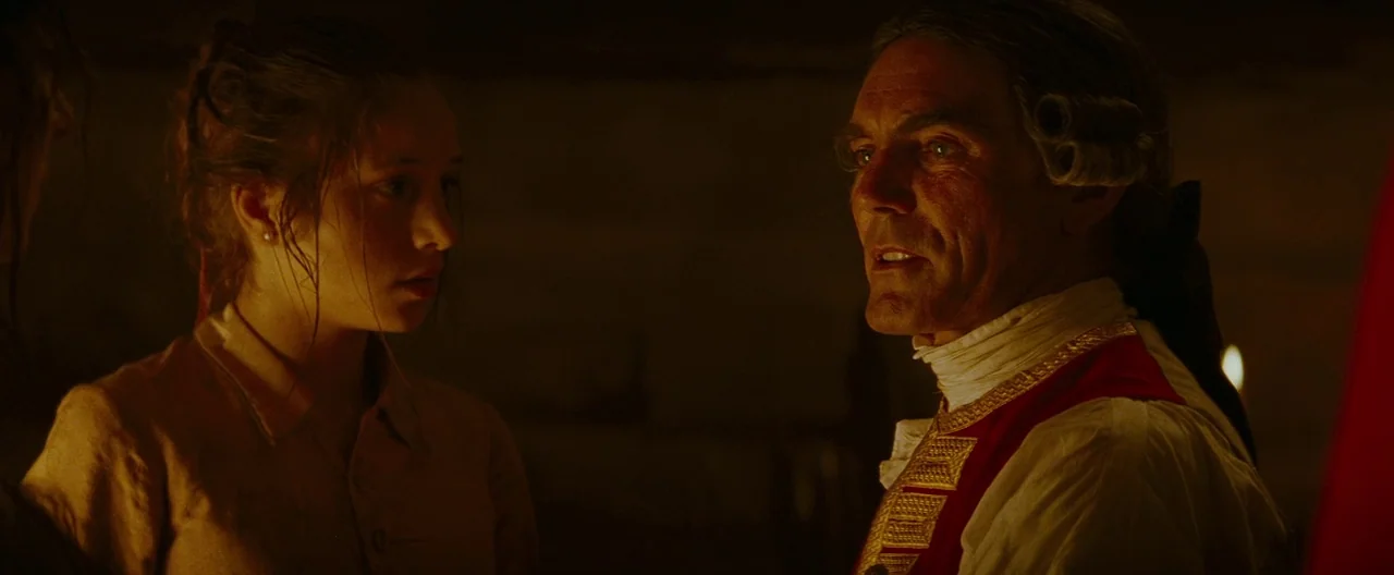 The Last of the Mohicans (1992) movie still: medium — A dark stone cellar is illuminated by a single warm candle flame. An older man in a red…