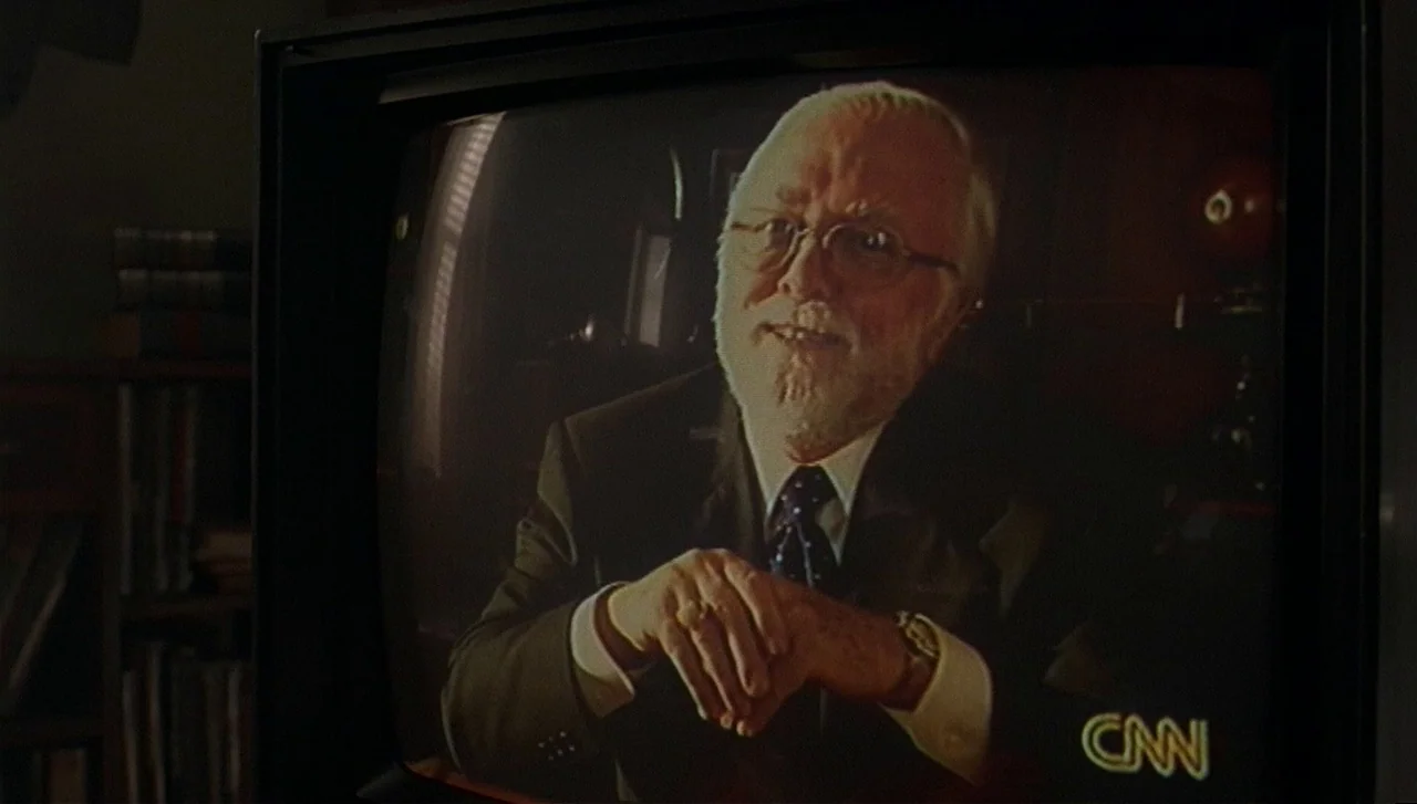 The Lost World: Jurassic Park (1997) movie still: closeup — An elderly man in a suit is displayed on an old CRT television screen. The subject…
