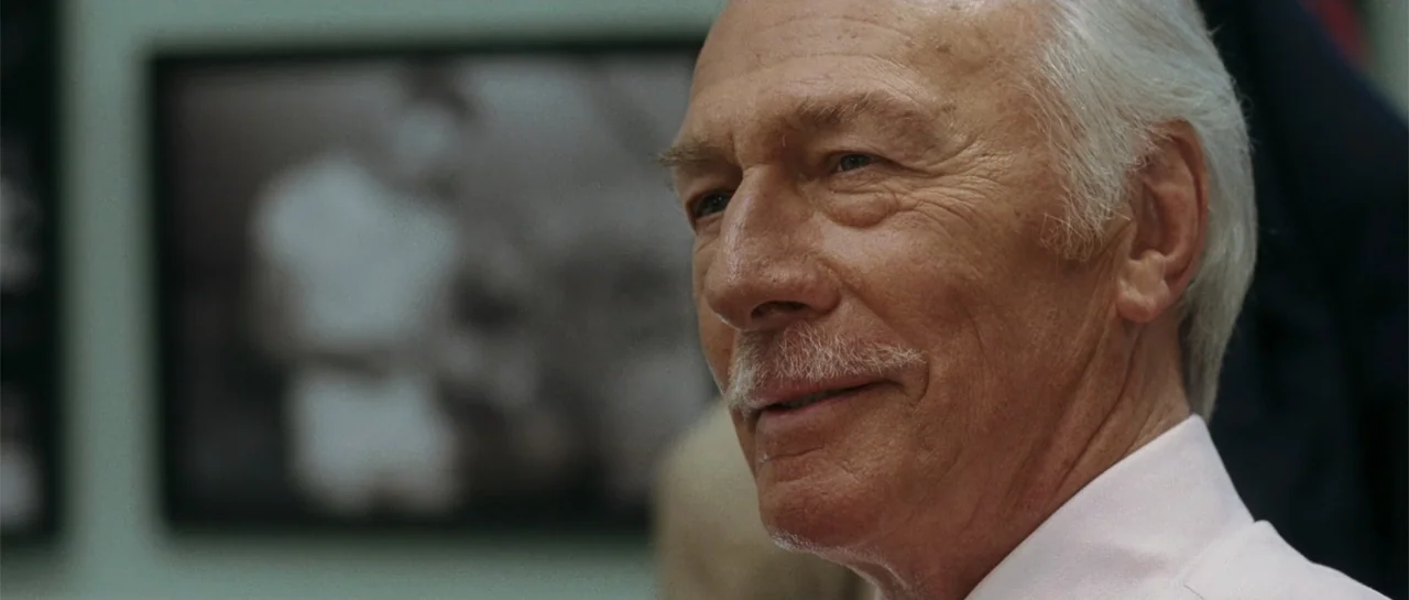 Inside Man (2006) movie still: closeup — An interior space features a light-colored wall with a framed black-and-white photograph. An elderly man…
