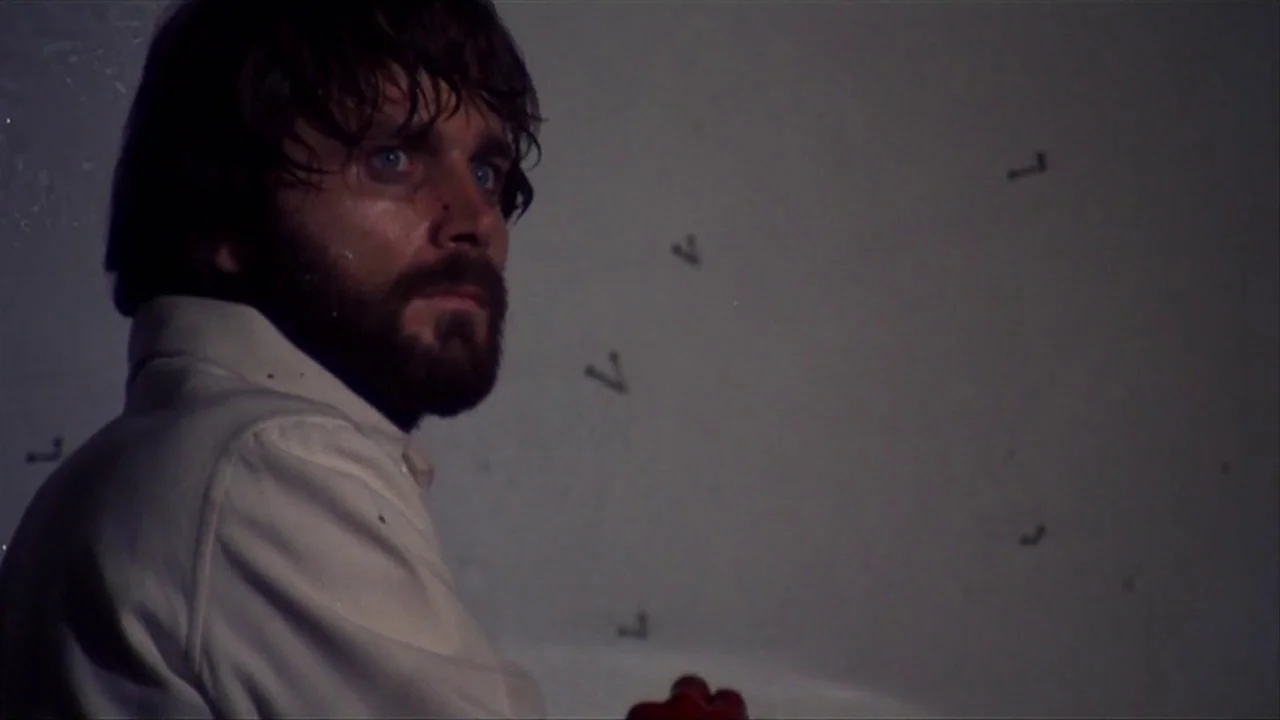A Quiet Place In The Country (1968) movie still: closeup — A dimly lit room with plain, off-white walls marked by small, scattered dark symbols. A…