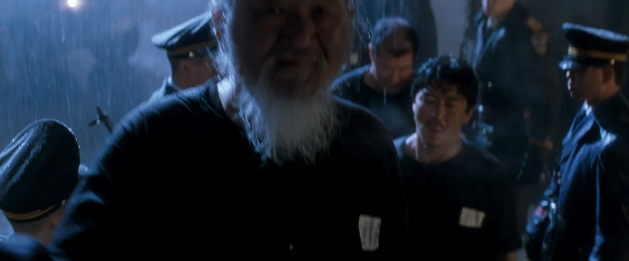 Lethal Weapon 4 (1998) movie still: medium — A dark outdoor space during a rainstorm filled with uniformed personnel. An elderly man with a white…