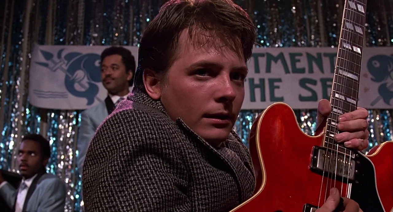 Back to the Future (1985) movie still: medium — A high school gym interior decorated with silver tinsel and an 'Enchantment Under the Sea' banner. A…