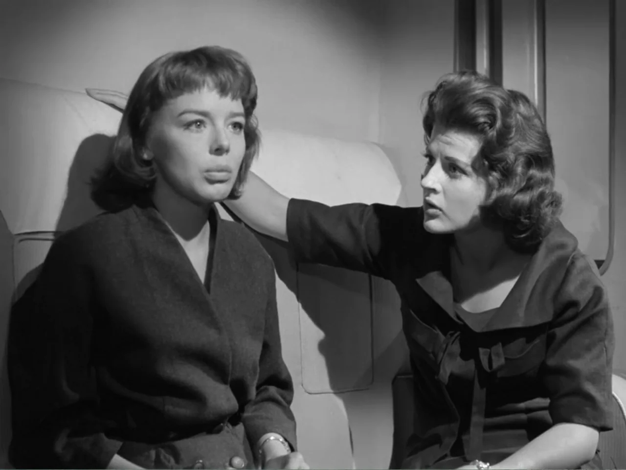 The Crawling Eye (1958) movie still: medium — Two women sit side by side in an airplane seat against a plain wall. One woman turns to speak to the…