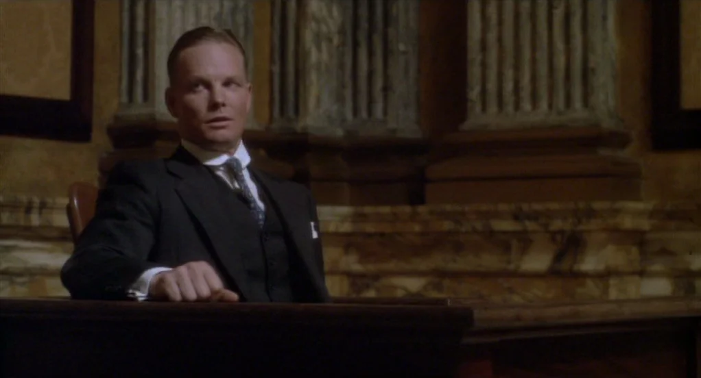 Eight Men Out (1988) movie still: medium — A man in a suit sits behind a polished wooden witness stand in a courtroom. Elaborate marble…