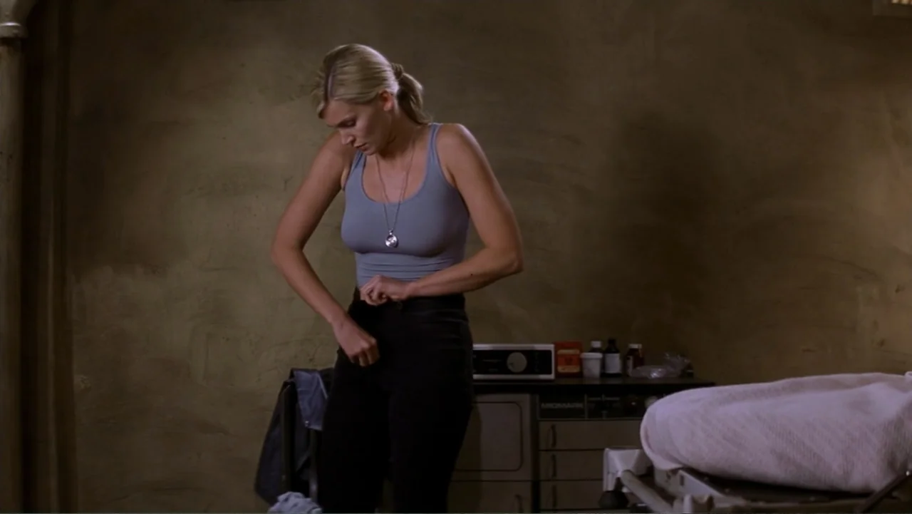 Ghosts of Mars (2001) movie still: medium — A clinical room with beige walls contains medical cabinetry and an examination table. A woman stands by…