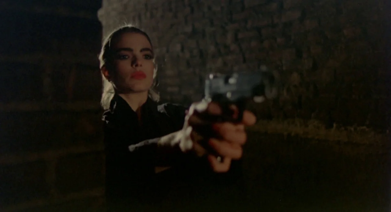 Ms. 45 (1981) movie still: medium — A dark, cramped space features a rough brick wall in the background. A young woman stands facing forward, aiming…