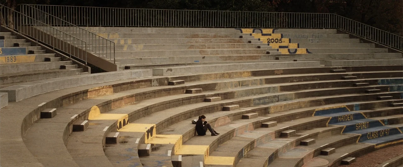 17 Again (2009) movie still: wide — A curved, weathered concrete stadium seating area features yellow and blue painted graduation year markers. A…