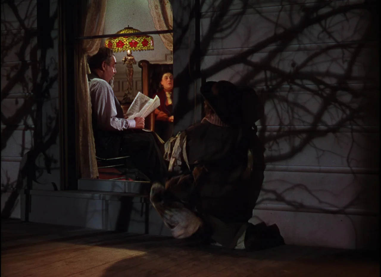Meet Me In St. Louis (1944) movie still: medium — A man sits reading a newspaper inside a brightly lit room at night. A person kneels on the…
