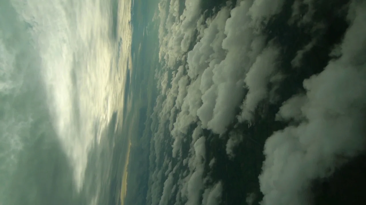 Counting (2015) movie still: establishing — A vast expanse of scattered cumulus clouds fills the frame under a bright sky. The perspective is tilted…