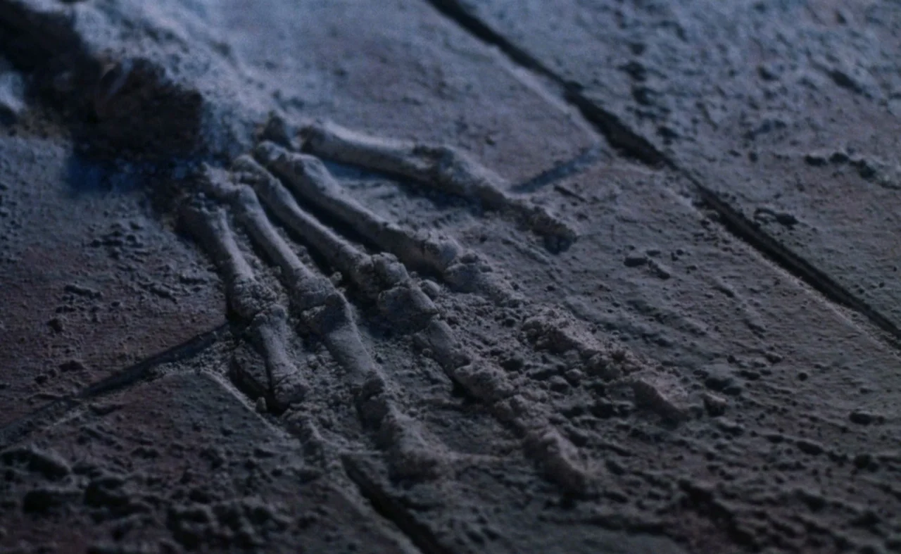 The Pit and The Pendulum (1991) movie still: closeup — A close-up view of a human skeletal hand lying flat on a dirt surface. The bones are…