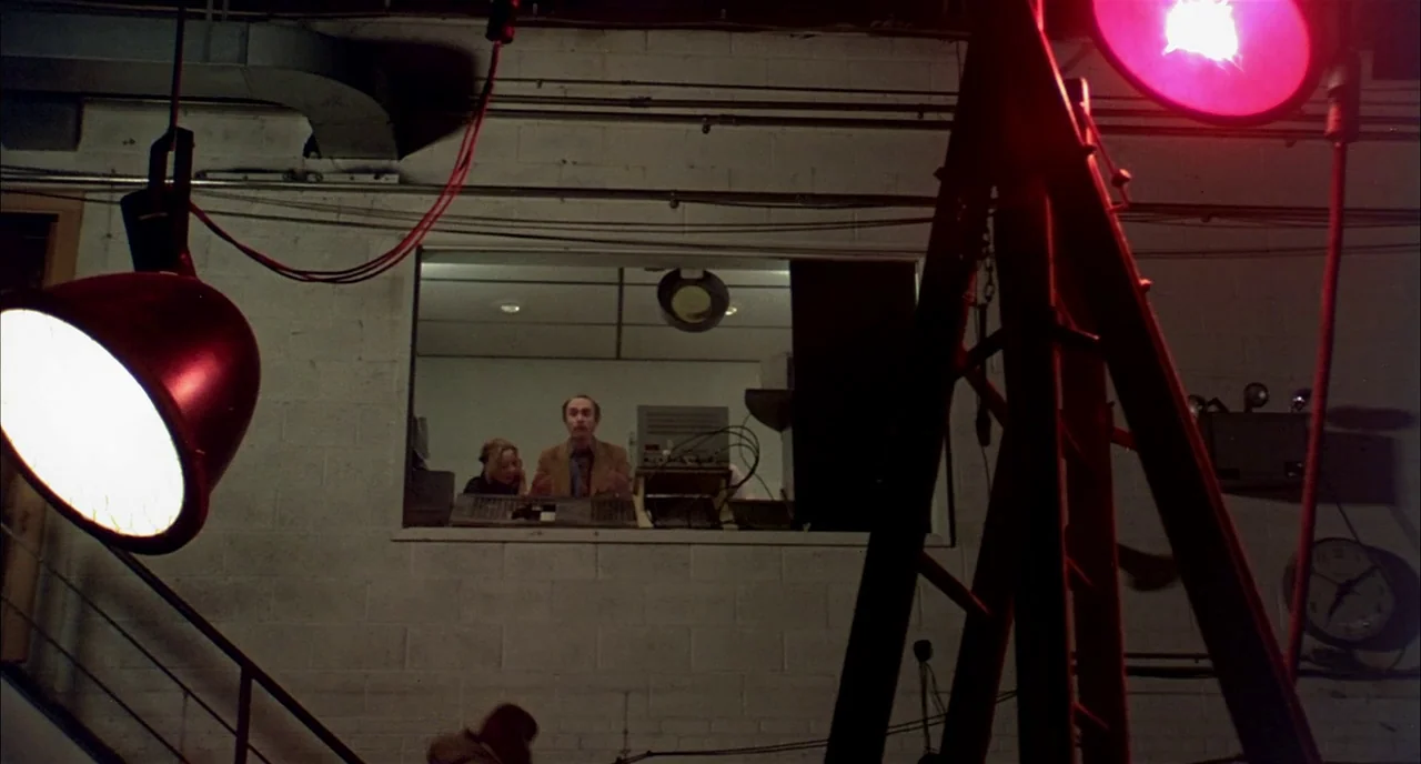 Dawn of the Dead (1978) movie still: wide — A white-painted cinder block room has a large rectangular observation window set into the wall. A man…