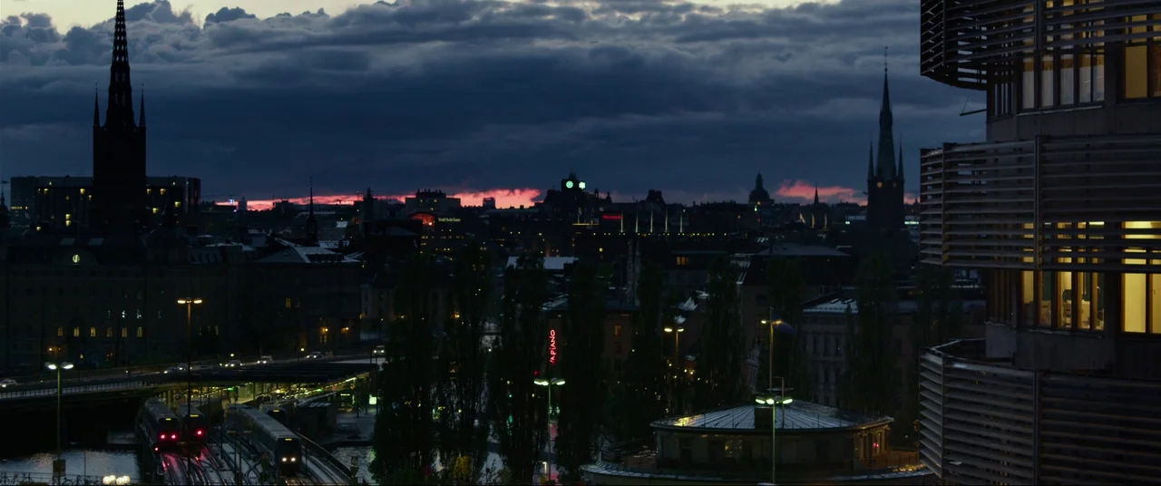 The Girl With The Dragon Tattoo (2011) movie still: establishing — A wide cityscape features traditional church spires silhouetted against a dark,…